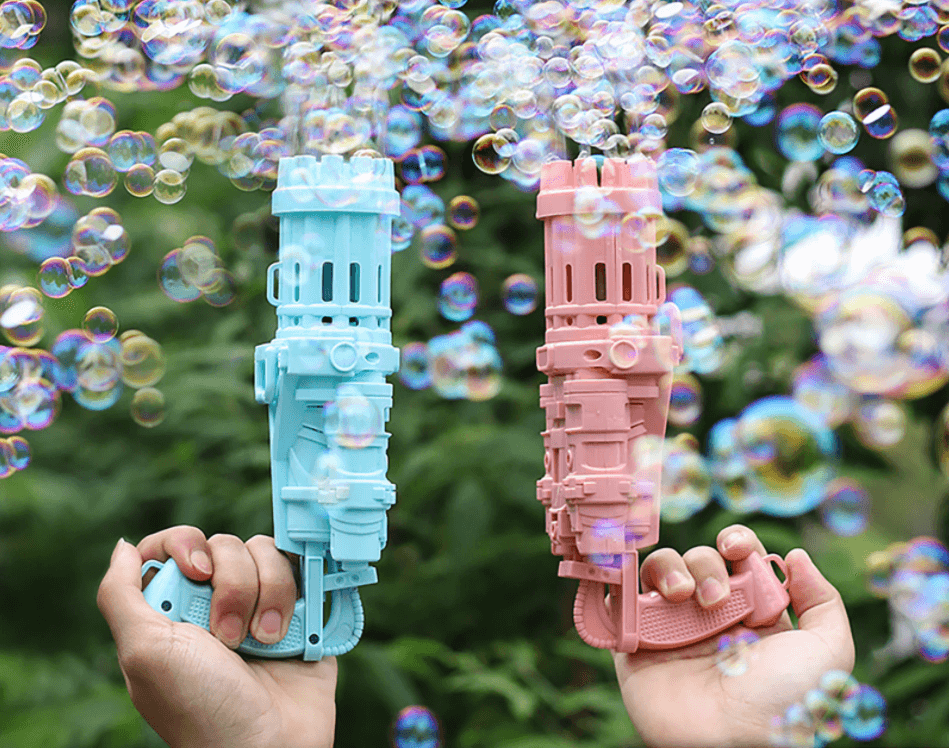 Glad flicka med automatisk bubbelpistol som sprutar bubblor, njuter av utomhuslek