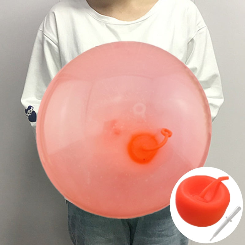 Två barn leker med en gigantisk uppblåsbar bubbelboll på gräsmattan, rolig sommarlek