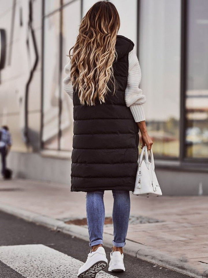 Kvinna bär en stilren, knälång damväst för dam. Lätt steppväst, idealisk som ytterplagg för en trendig look.