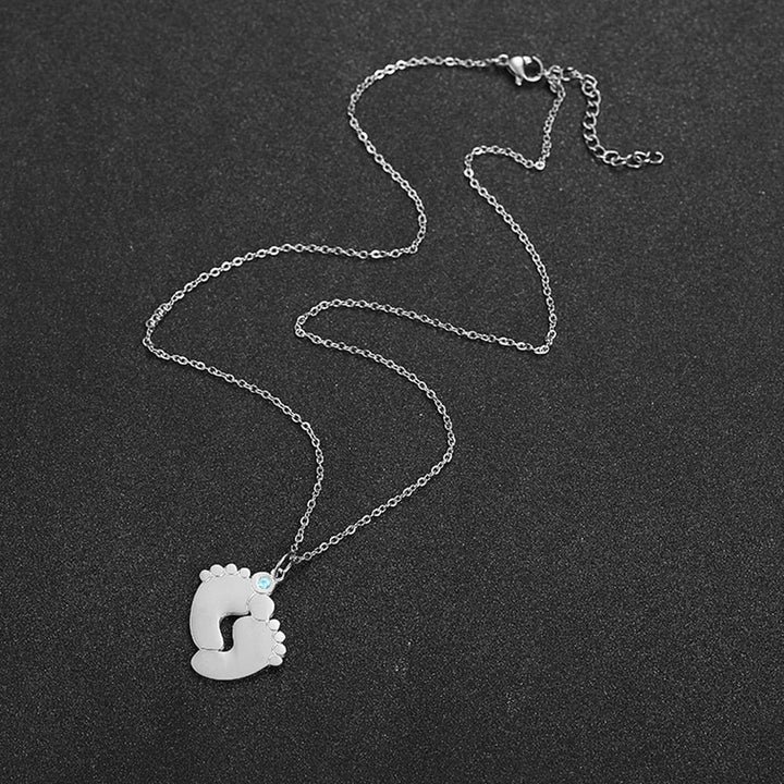 Närbild av personligt damhalsband med barnfötter, graverade namn & månadssten. Fin present till mamma.