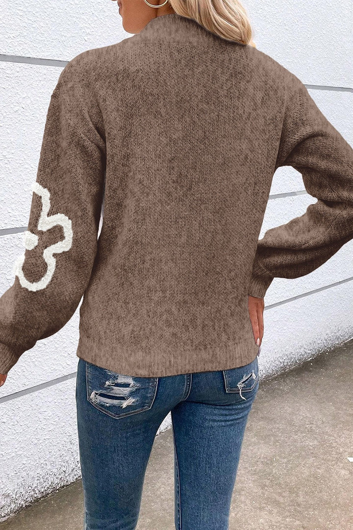 Detaljerad bild av en damtröja med intrikat blommotiv, bekväm halvdragkedja och avslappnad passform.