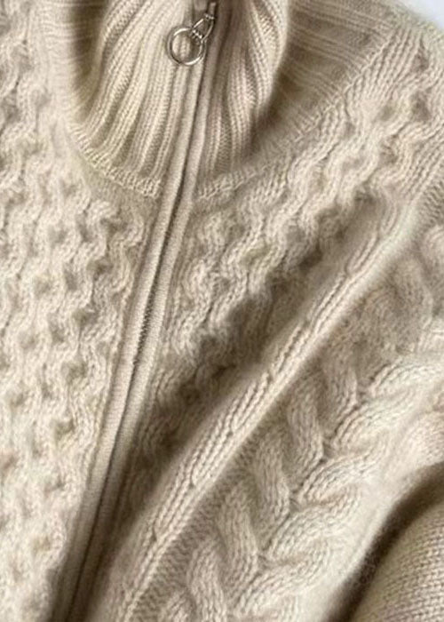 Detaljbild på beige stickad damkappa med silverfärgad dragkedja. Ett trendigt och bekvämt ytterplagg i ullblandning.