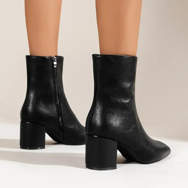 Detalj av kvinnors fötter i svarta damankelboots med blockklack och spetsig tå.