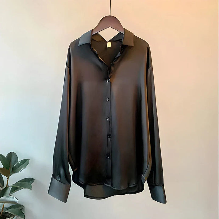 Modell som bär en damblus i silkesstil med långa ärmar i en vårig miljö.