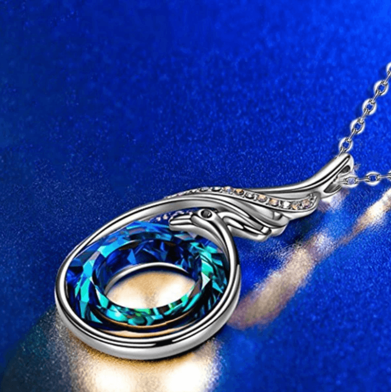 Unikt fenixhalsband med detaljerade vingar och glittrande blåa & gula kristaller. Symboliskt damsmycke.