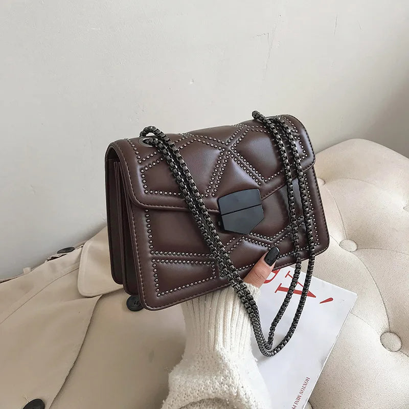 Trendig svart crossbody handväska för kvinna, med dekorativa nitar och kedjerem.