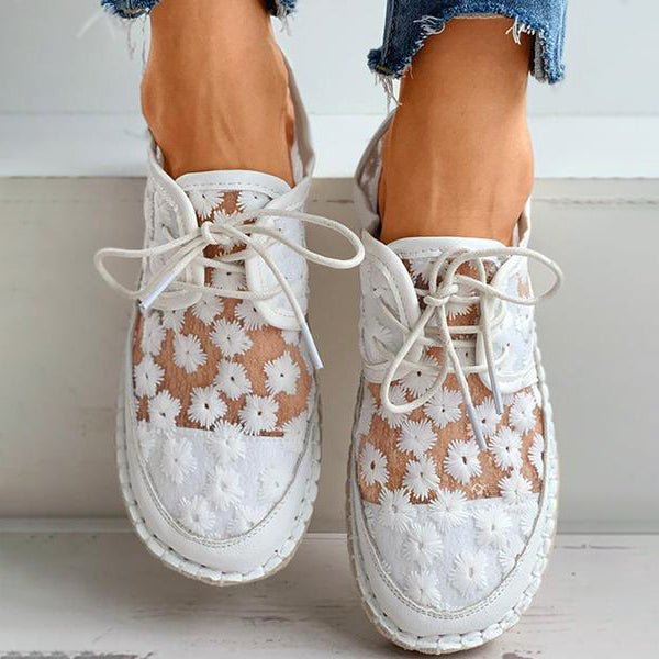Detaljbild av de broderade mönstren på kvinnors vita sneakers, ger en unik och stilren look.