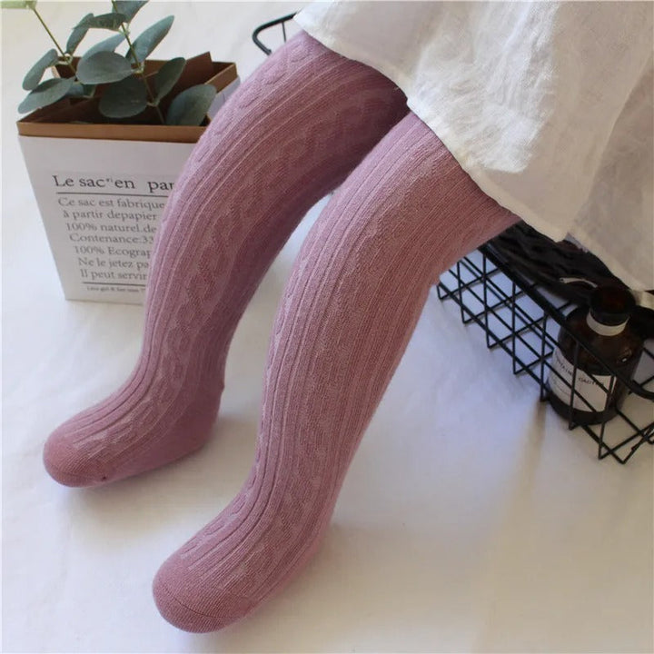 Flickors stretchiga kabelstickade strumpbyxor i bomull som hänger på tork, visar elasticitet.