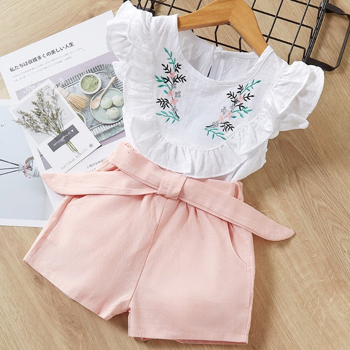 Flickors sommaroutfit: Prickiga shorts och vit casual skjorta, perfekt för soliga dagar, barnkläder.