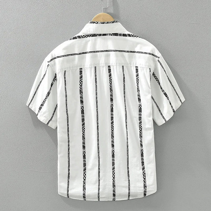 Man bär en vit och svart randig herrskjorta med korta ärmar, kombinerad med ljusa byxor, idealisk för sommaren.