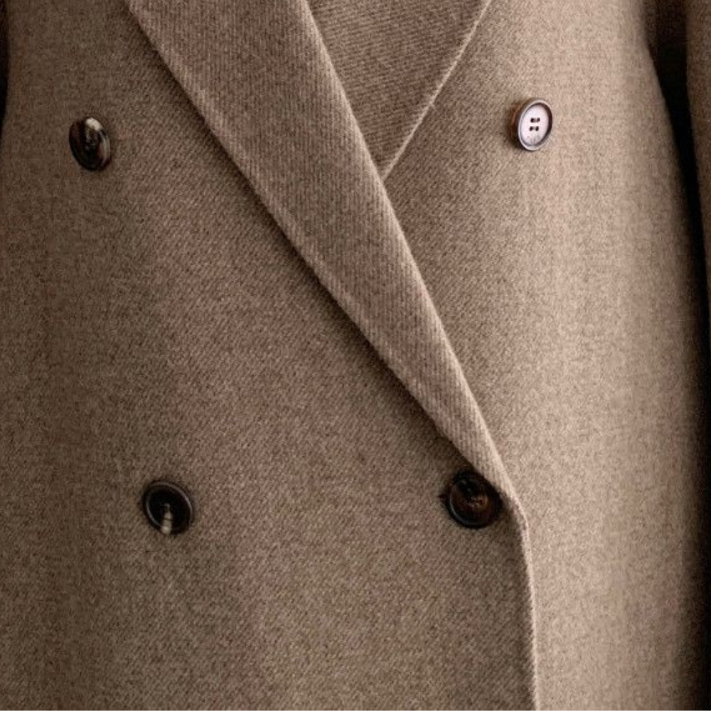 Kvinnors eleganta vinterkappa i klassisk beige, dubbelknäppt modell. Ett stilrent och värmande ytterplagg.