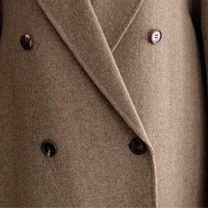 Kvinnors eleganta vinterkappa i klassisk beige, dubbelknäppt modell. Ett stilrent och värmande ytterplagg.