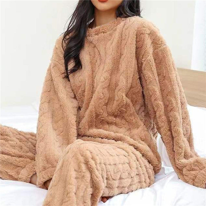 Ung kvinna läser bok i en beige fleecepyjamas vid en öppen spis. Vinter pyjamas för hemma.