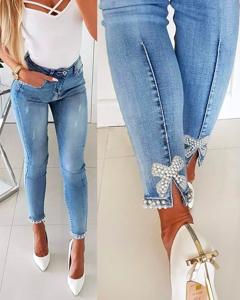 Detaljbild av blåa kvinnors denimbyxor som visar unika pärlor och en modeinriktad bågknut vid midjan, smickrande passform.
