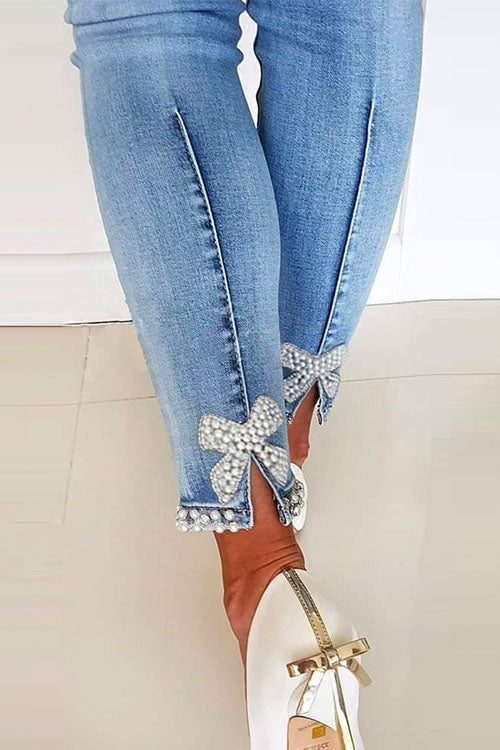 Modell bär blåa kvinnors denimbyxor med hög midja, pärlor och bågknut, framhäver smickrande figurnära passform och stil.