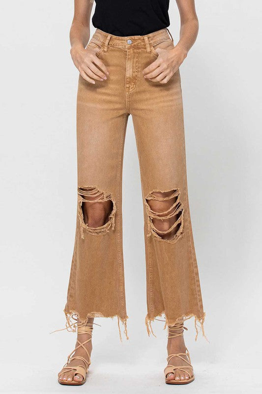 Detaljbild på guldfärgad knapp och dragkedja på bekväma crop flare jeans för kvinnor i 90-talsstil, studiobild.