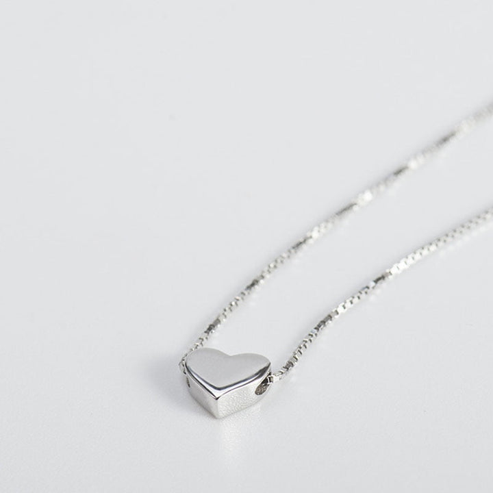 Närbild på minimalistiskt silverfärgat hjärthalsband för dam. Subtilt kärlekssmycke med tunn kedja.