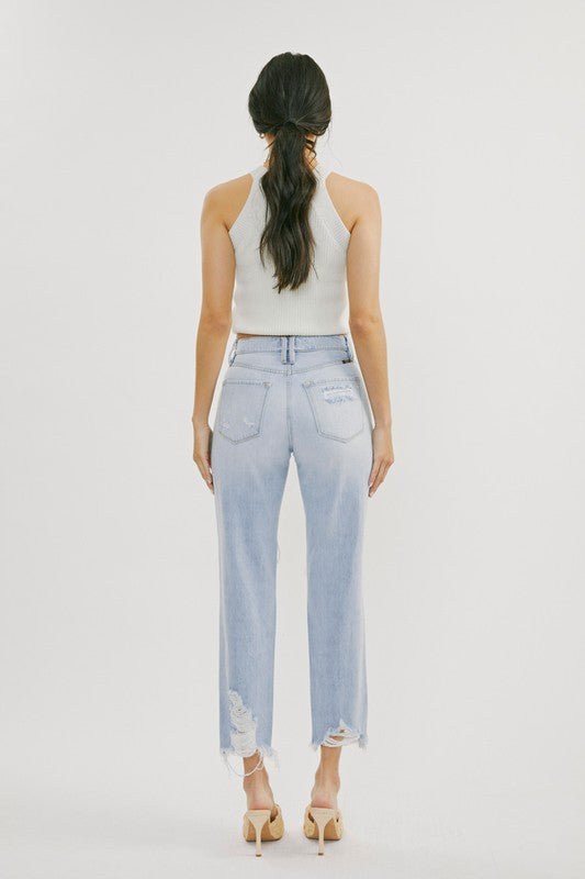 Högmidjade jeans i ljus denim med strategiska distressade områden för kvinnor, fotograferade liggandes. Vardagskläder.
