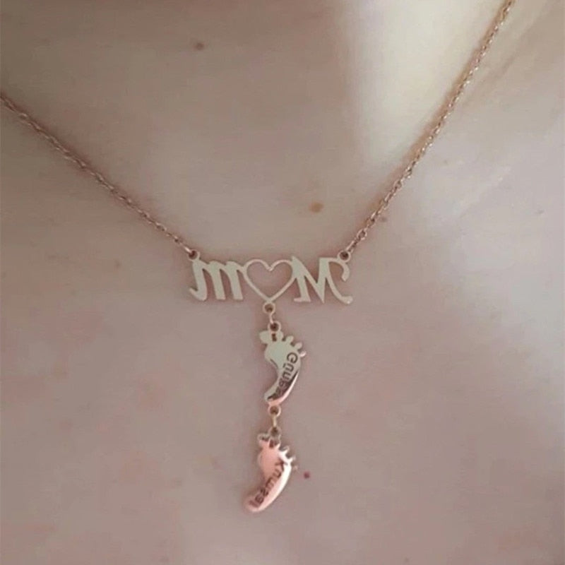 Detaljer av mammahalsband med babyfötter och gravyr av namn. Ett kärt minne i silver, guld eller roséguld.
