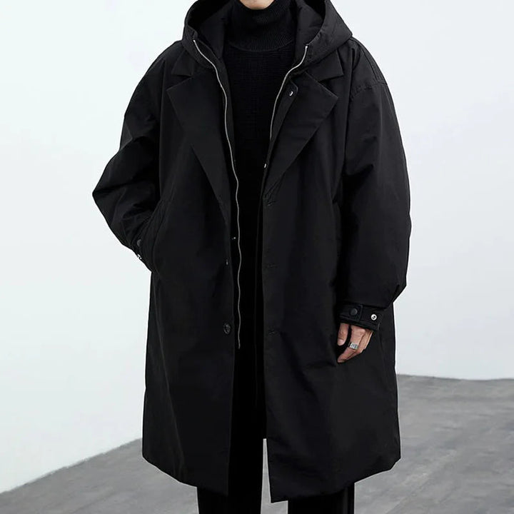 Helkroppsbild av en man som bär en modern svart trenchcoat med huva. Stilren och avslappnad herrjacka.