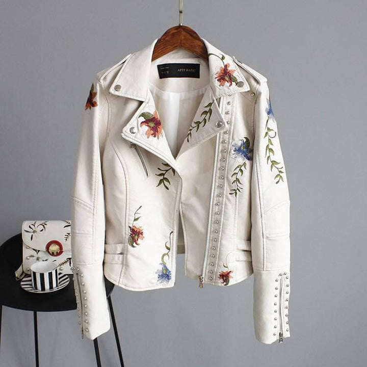 Närbild av textur på konstläderjacka med inslag av blommig broderi i svart och beige.