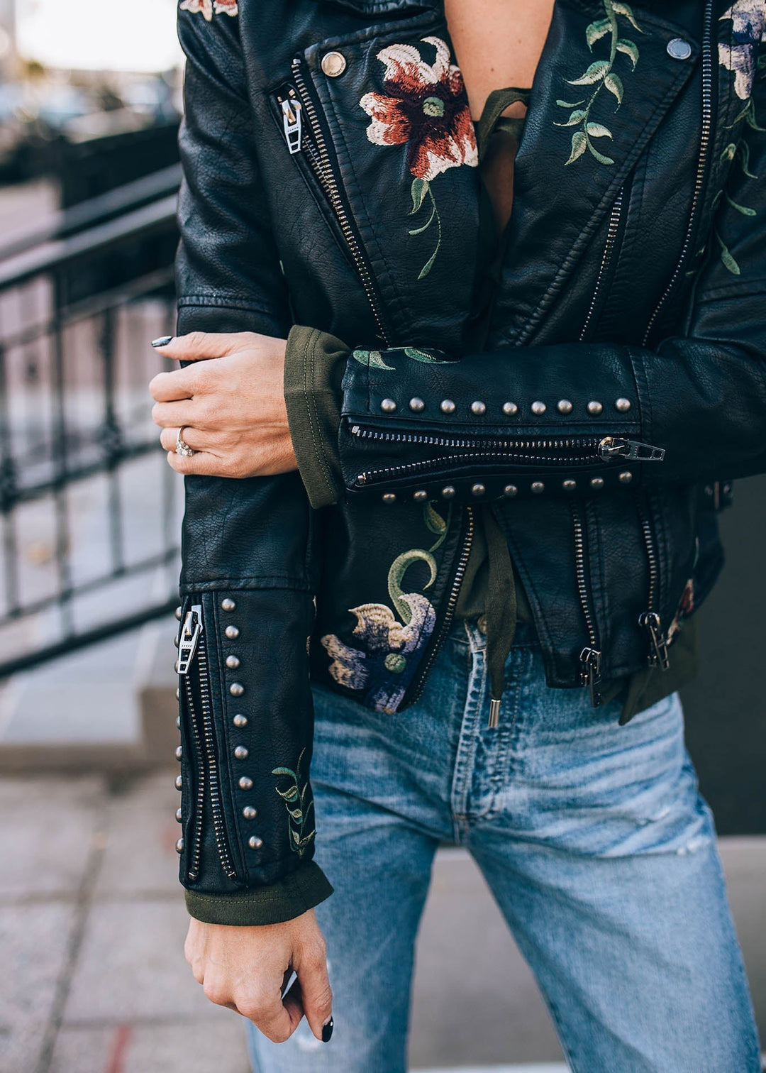 Modell bär beige damjacka i konstläder med blommig broderi, en chic asymmetrisk jacka.