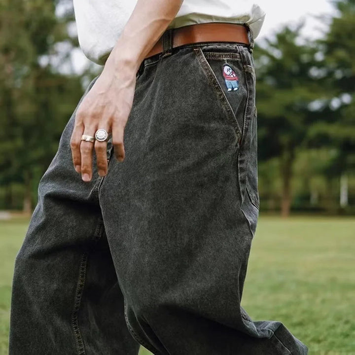 Närbild av svarta baggy herrjeans, visar tygets kvalitet och de vida benens rymliga design.