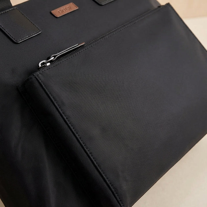 Person bär MetroBrief unisex laptopväska i canvas. Stilren datorväska för kontor, resor & daglig pendling.