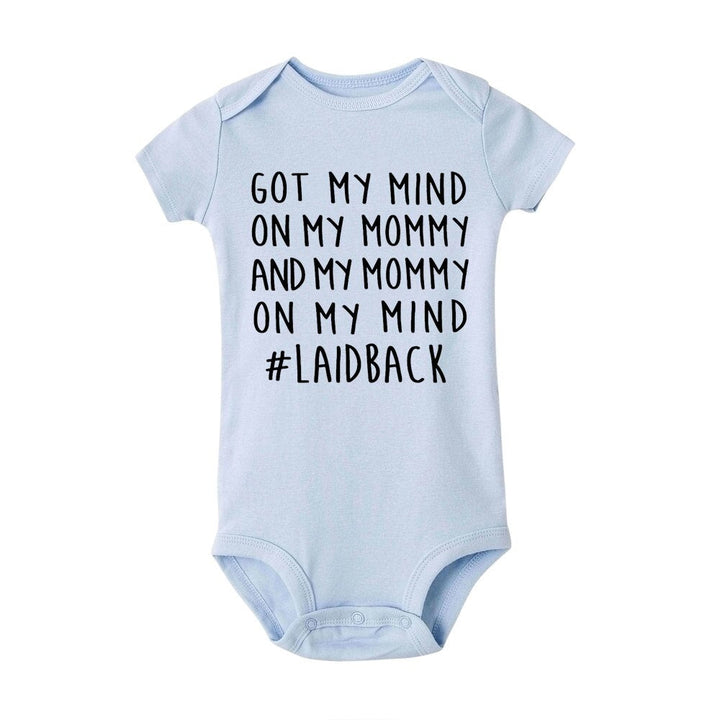Bebis som ligger på mage iförd vit babybody med unikt mammabudskap-tryck, bekväm barnmode.